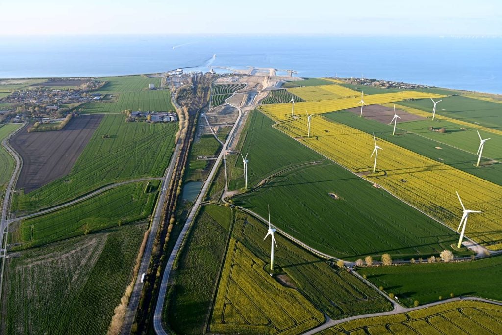 An aerial image of the beginning of construction in Puttgarden next to a highway and wind turbines in fields